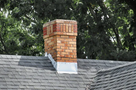 Two-tone brick chimney with new flashing among trees